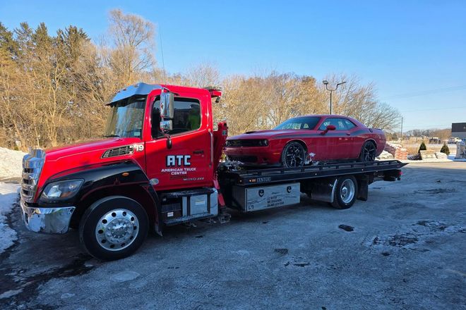 Red tow truck transporting a red Dodge Challenger on a snowy day.