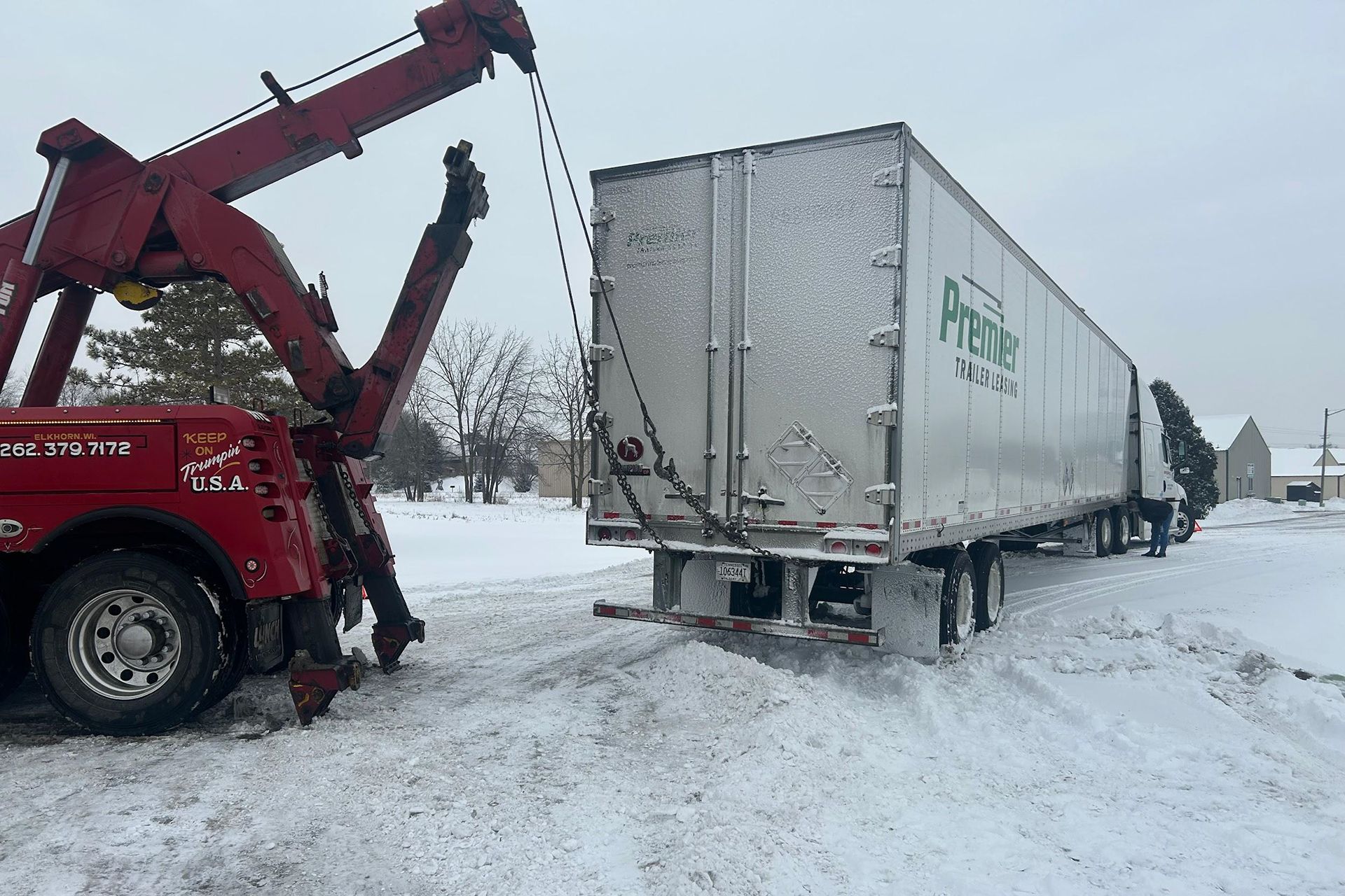 Tow truck pulling a semi-trailer out of the snow on a snowy day.
