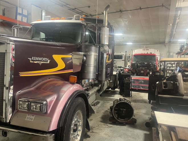 Semi-truck being repaired in a garage; a transmission sits on the floor.