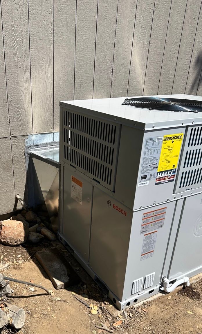 A large air conditioner is sitting in the dirt next to a wall