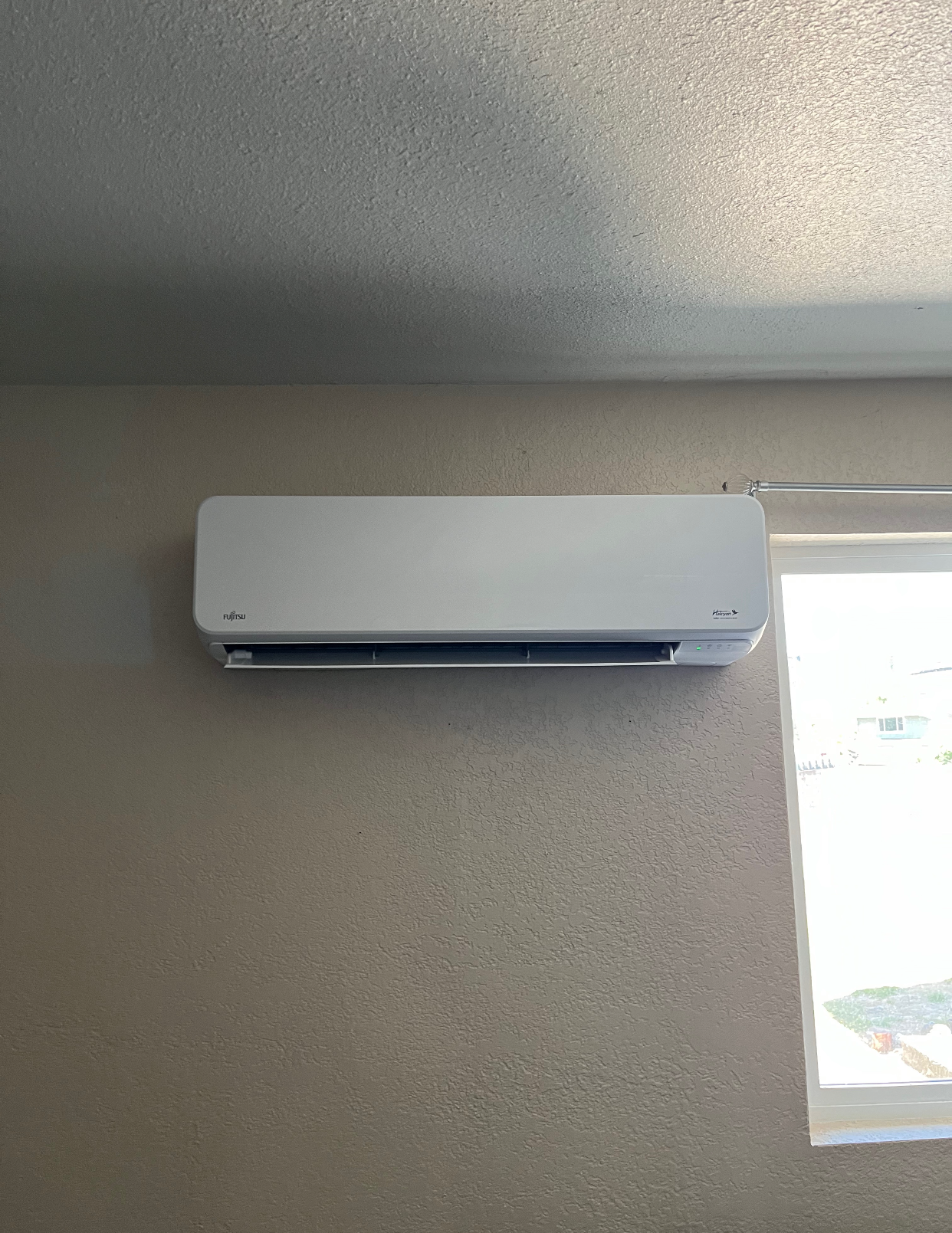 A white air conditioner is hanging on a wall next to a window
