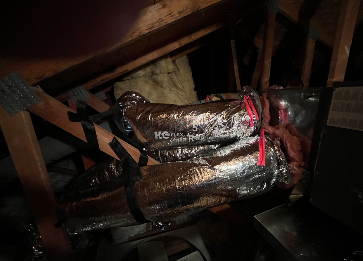 A bunch of ducts are hanging from the ceiling of an attic