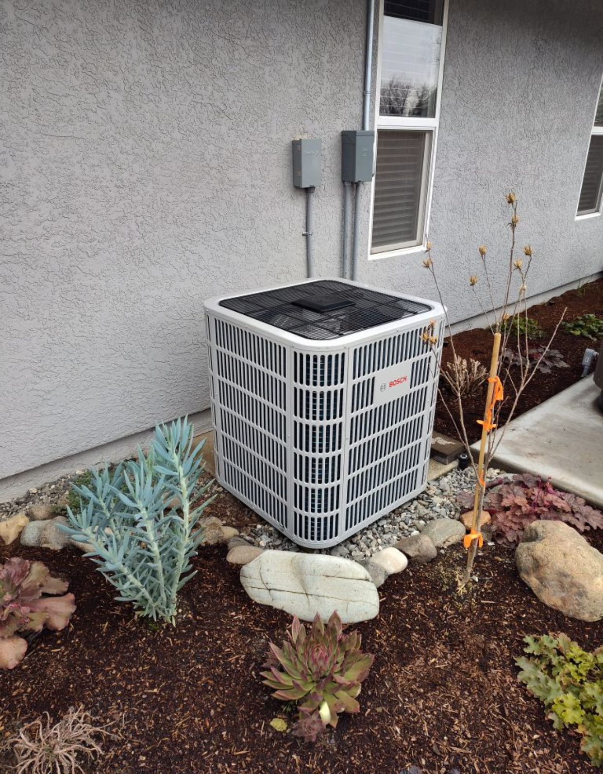 An air conditioner is sitting in a garden next to a house