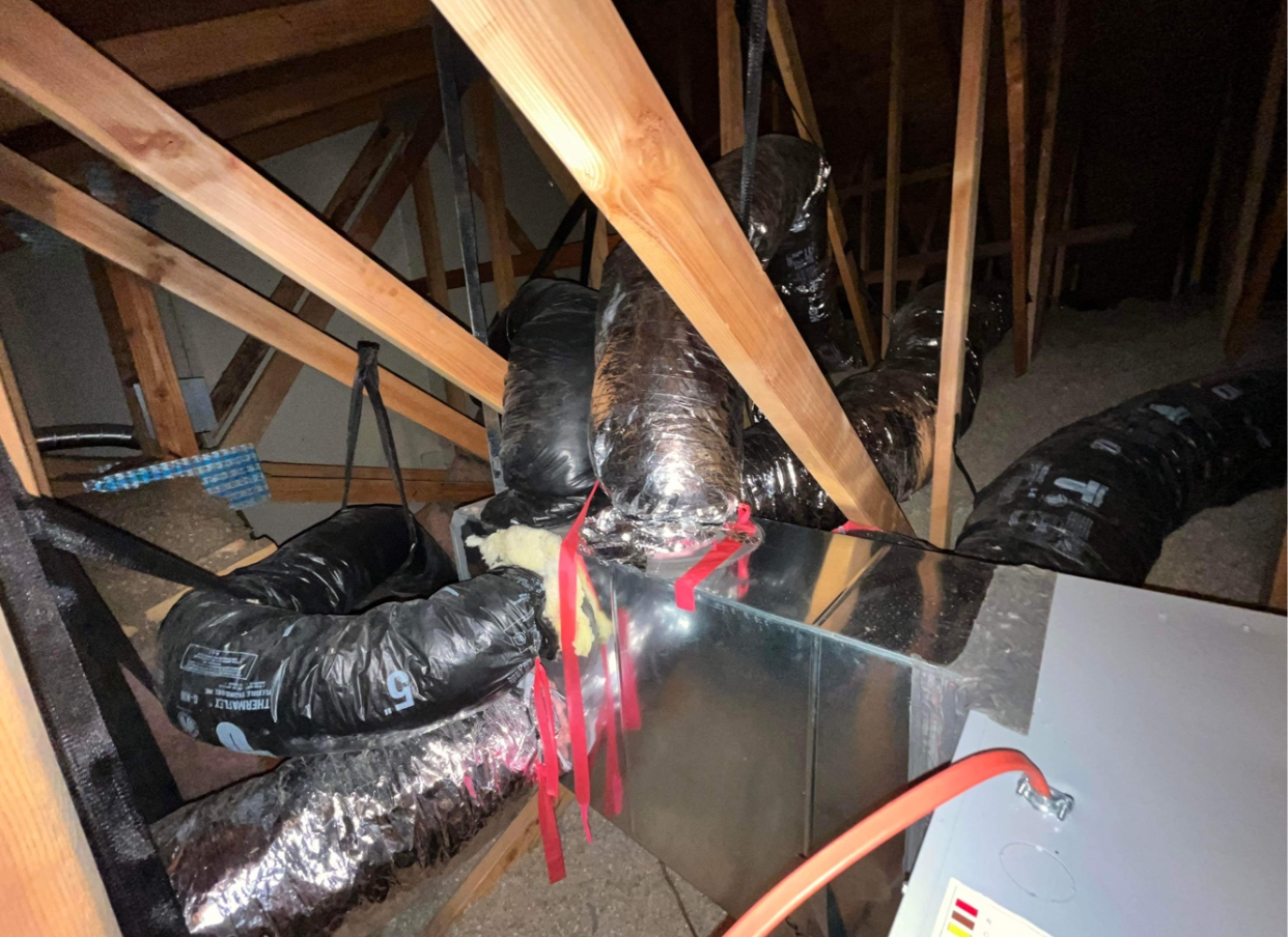 A bunch of ducts are hanging from the ceiling of an attic