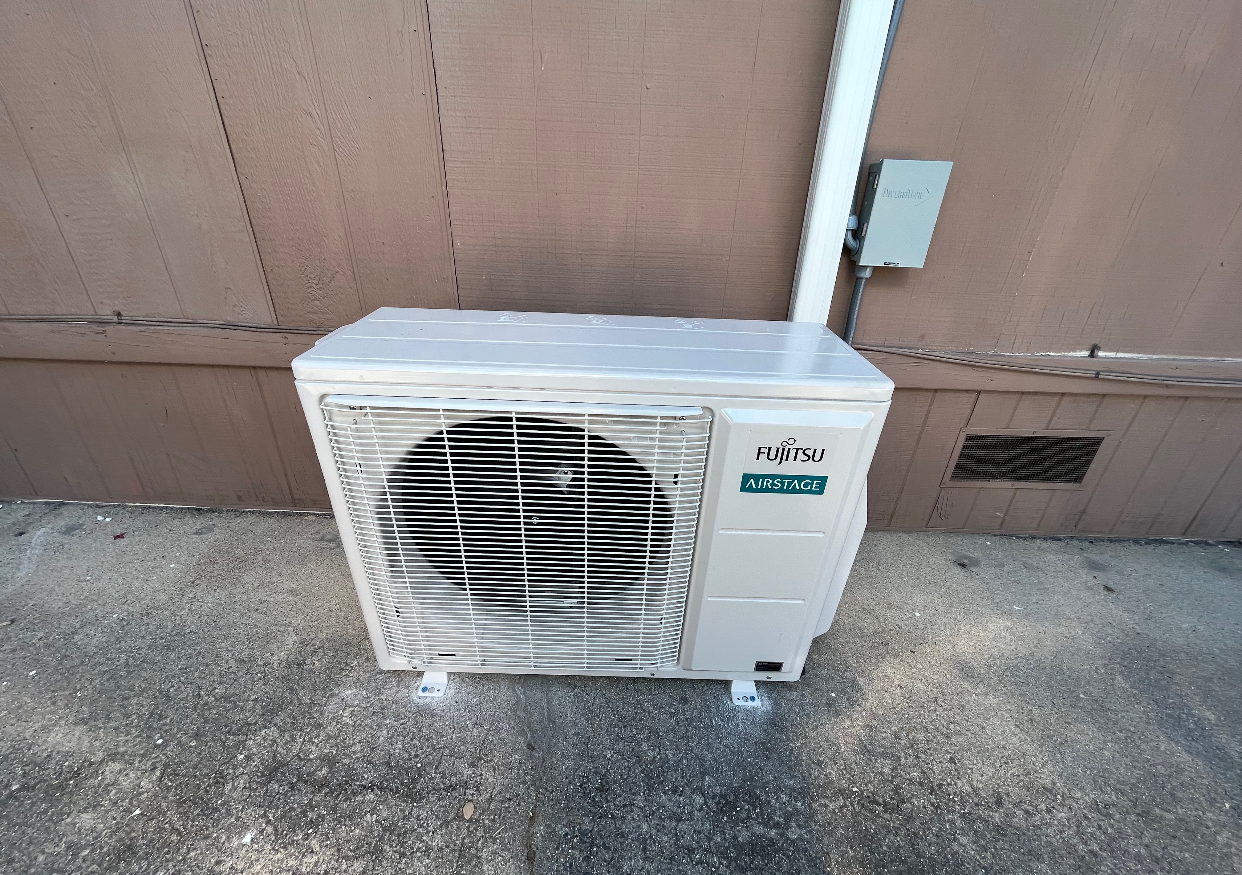 A white air conditioner is mounted to the side of a building