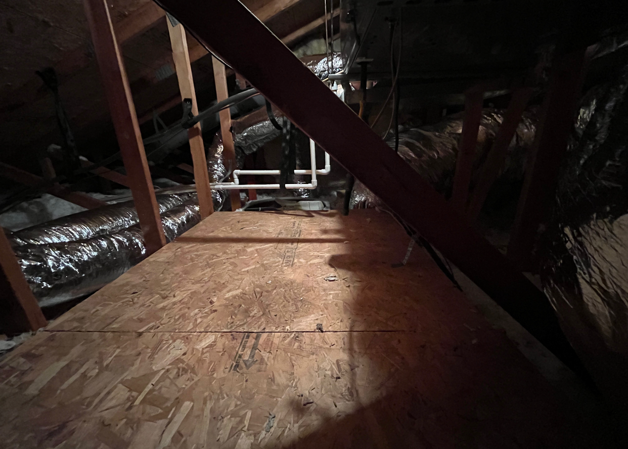 A dark attic with a wooden floor and a staircase