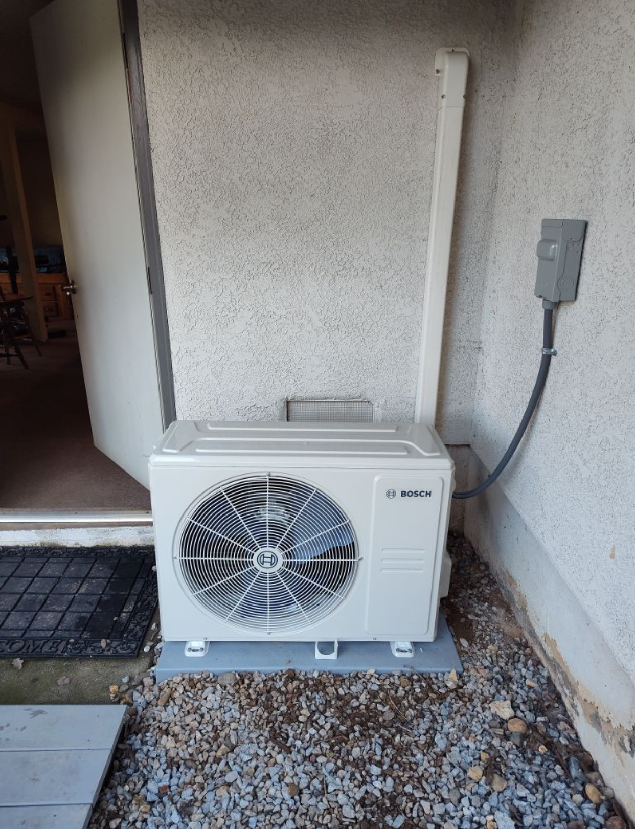 A white air conditioner is sitting outside of a building next to a door