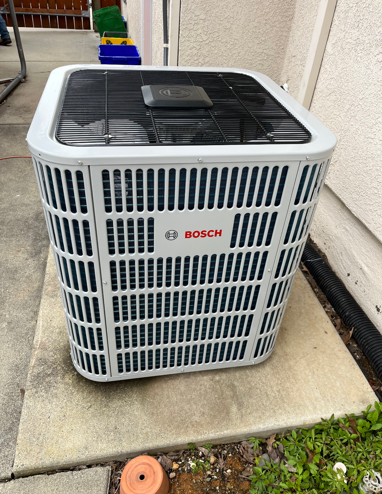 A bosch air conditioner is sitting on a sidewalk next to a building