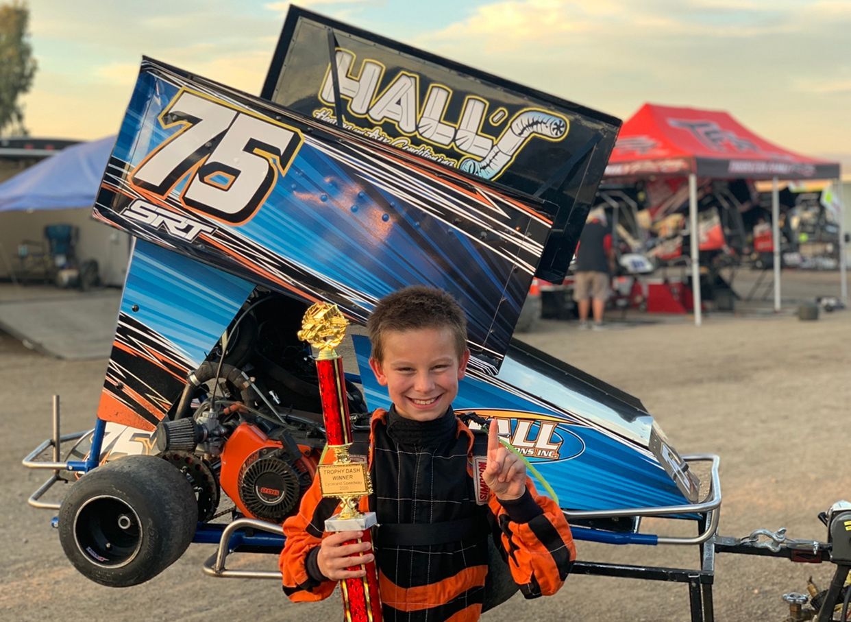A young boy is holding a trophy in front of a race car
