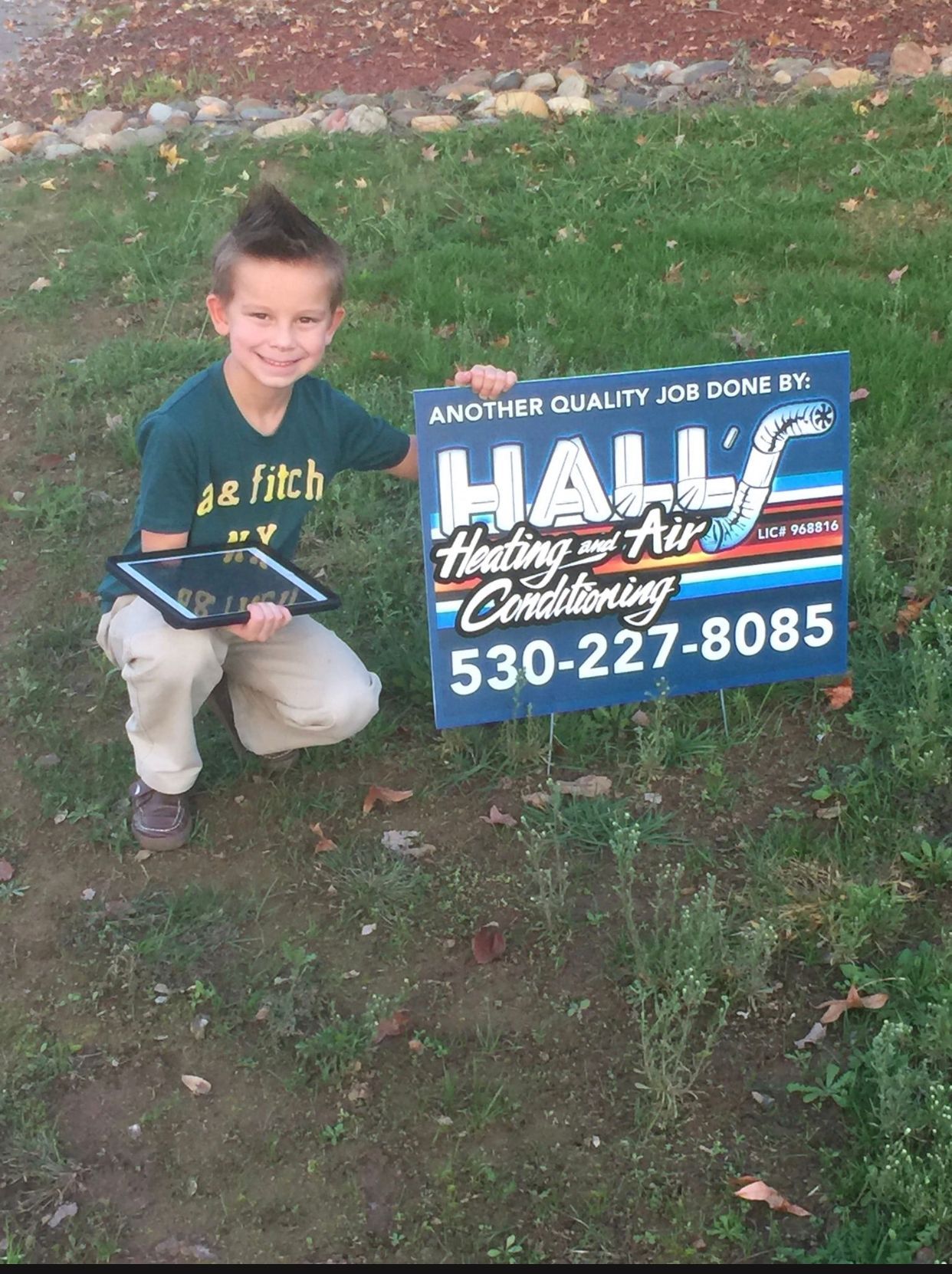 A young boy is kneeling holding a sign for hall heating and air conditioning