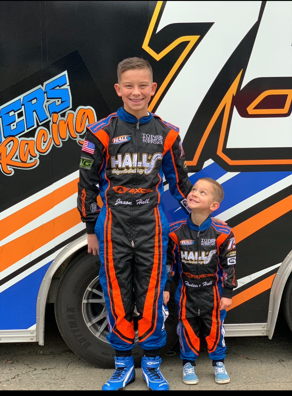 Two young boys are standing next to each other in front of a race car