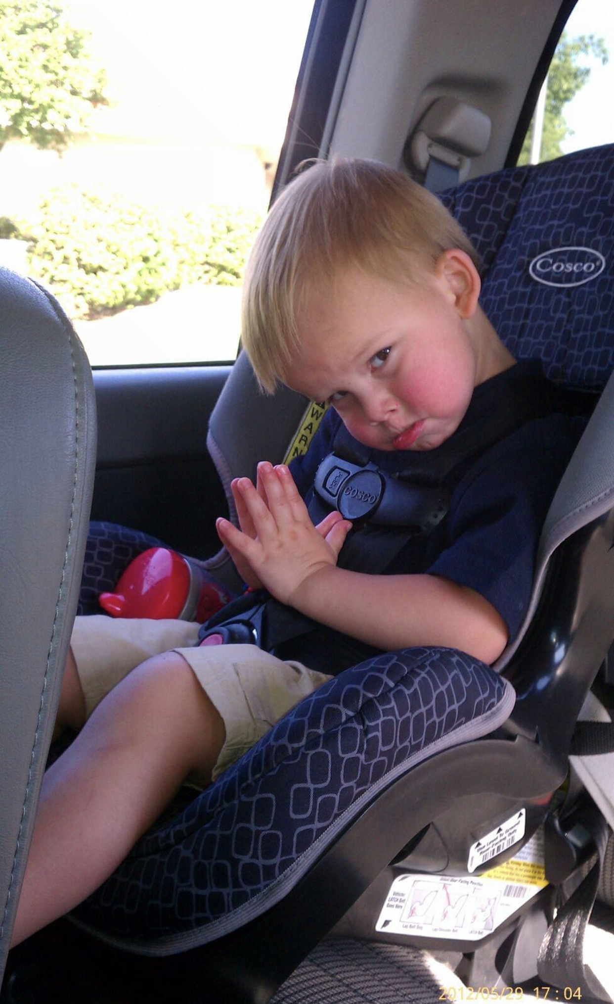 A young boy is sitting in a car seat and making a funny face