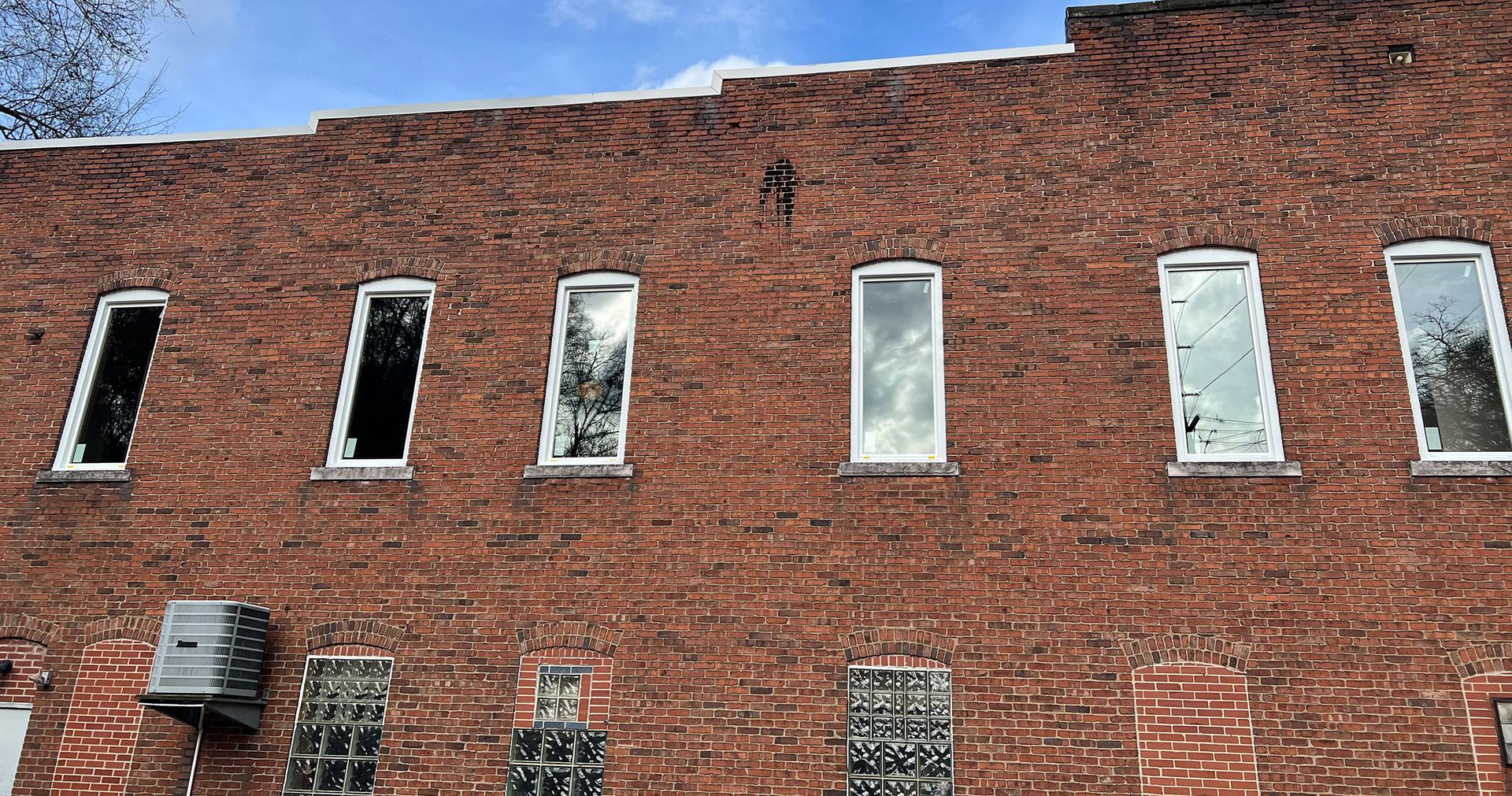 Red brick building with six narrow, white-framed windows. A/C unit on the left side.