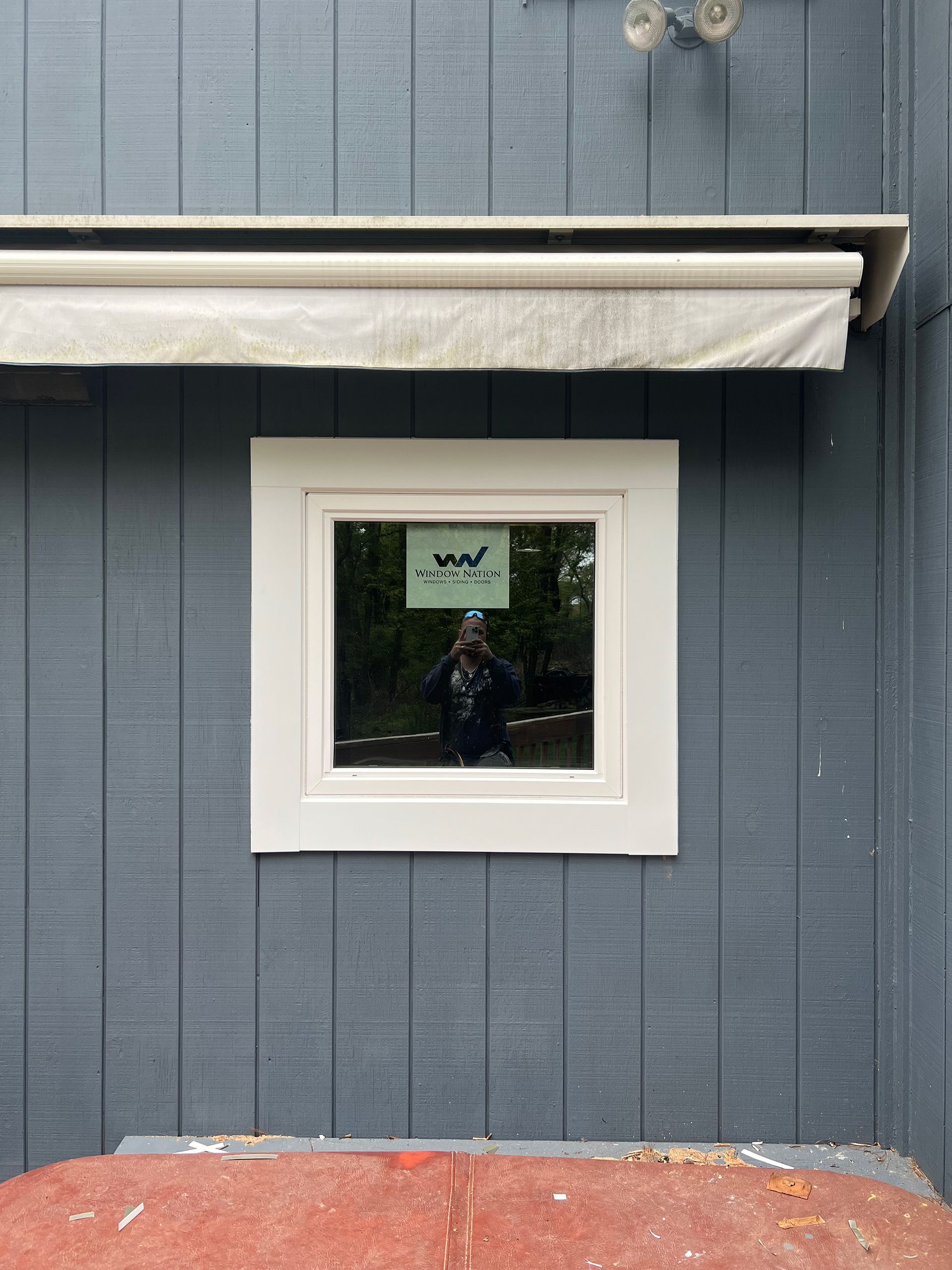 Window with white trim on a blue-gray wall; a person is reflected in the glass.