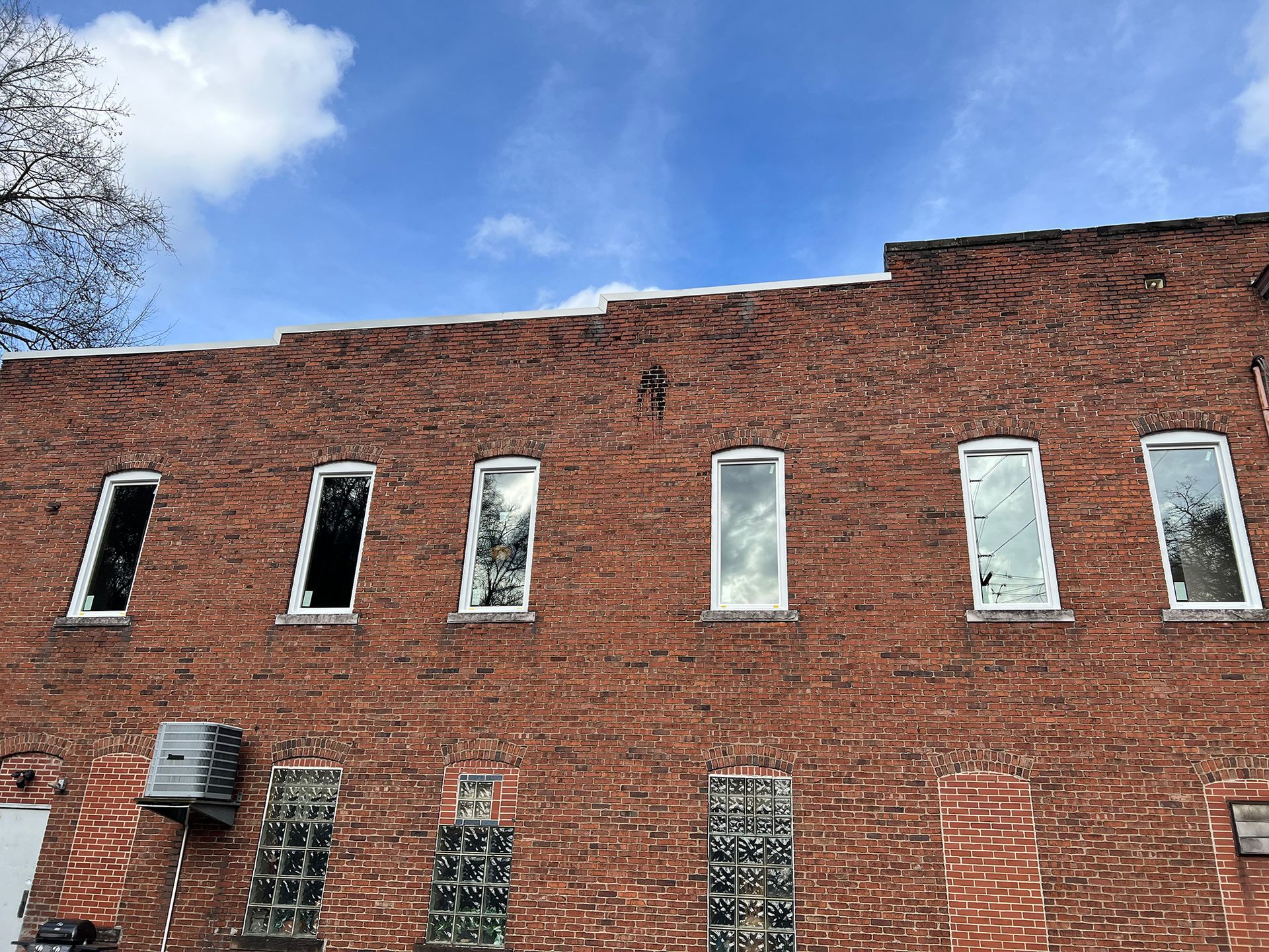 Red brick building with a row of rectangular windows, clear sky, and some snow on the roof.