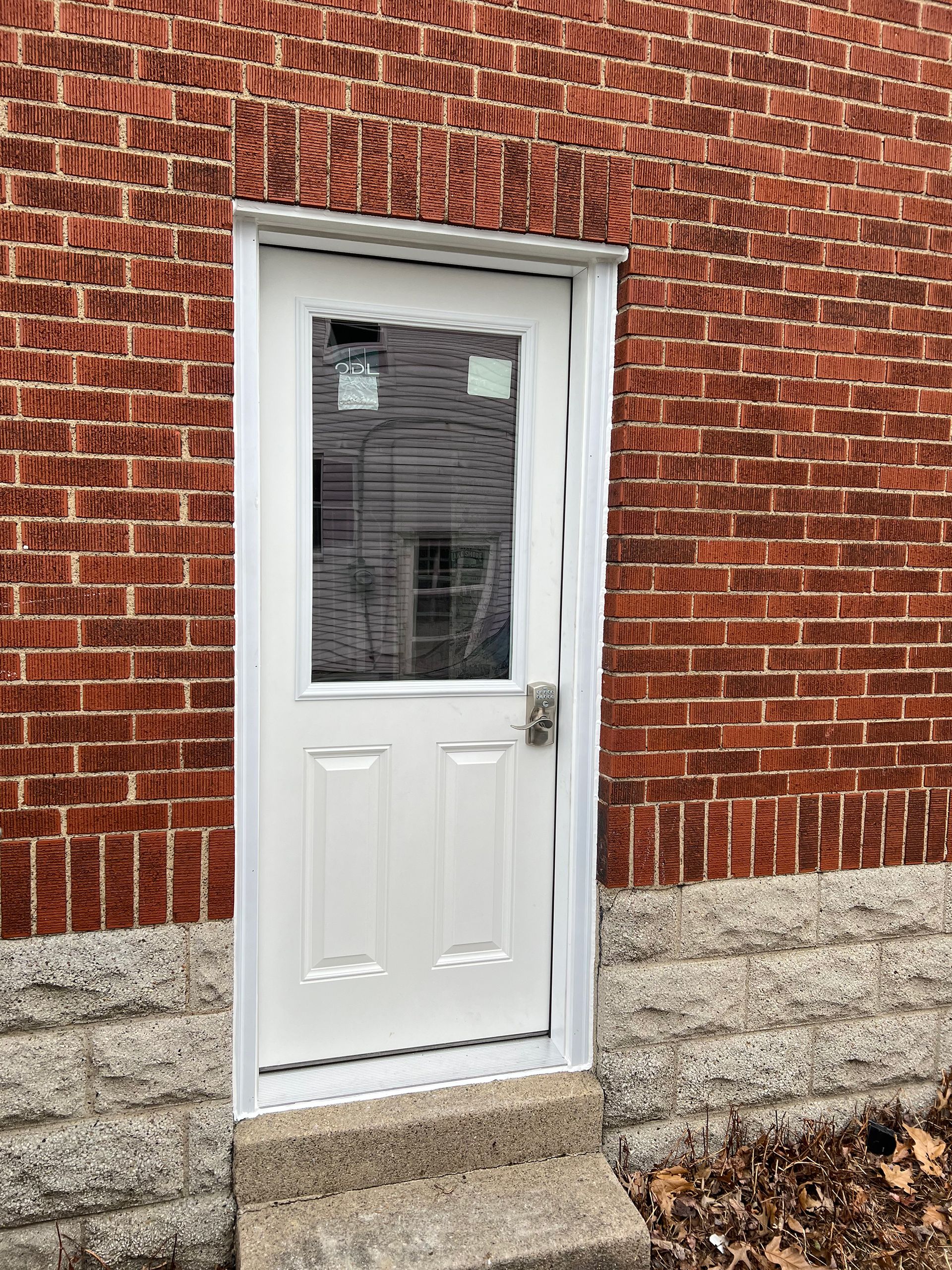 White door with glass panel set in a red brick building, small concrete steps below.