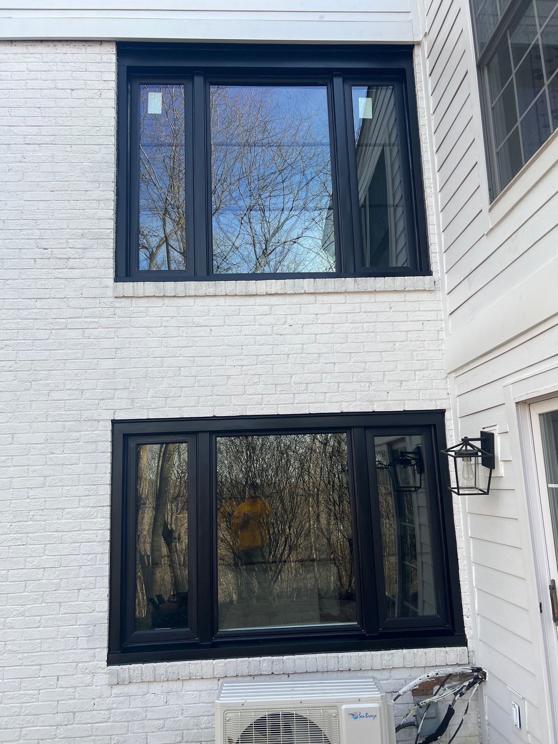 Black-framed windows on a white brick building, reflecting trees. Air conditioning unit below lower window.