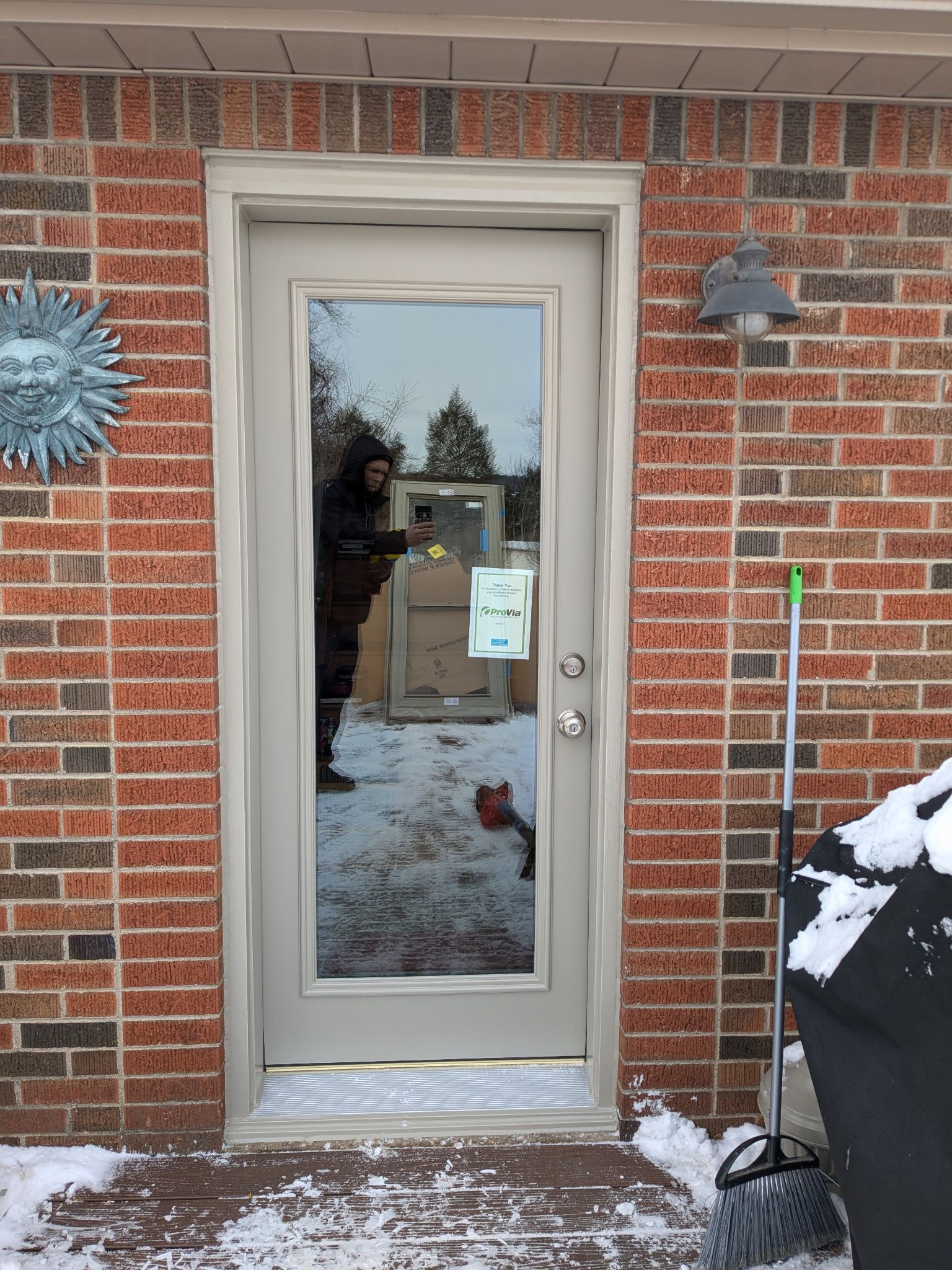 Glass door in brick wall with snowy ground. Person reflected in door.