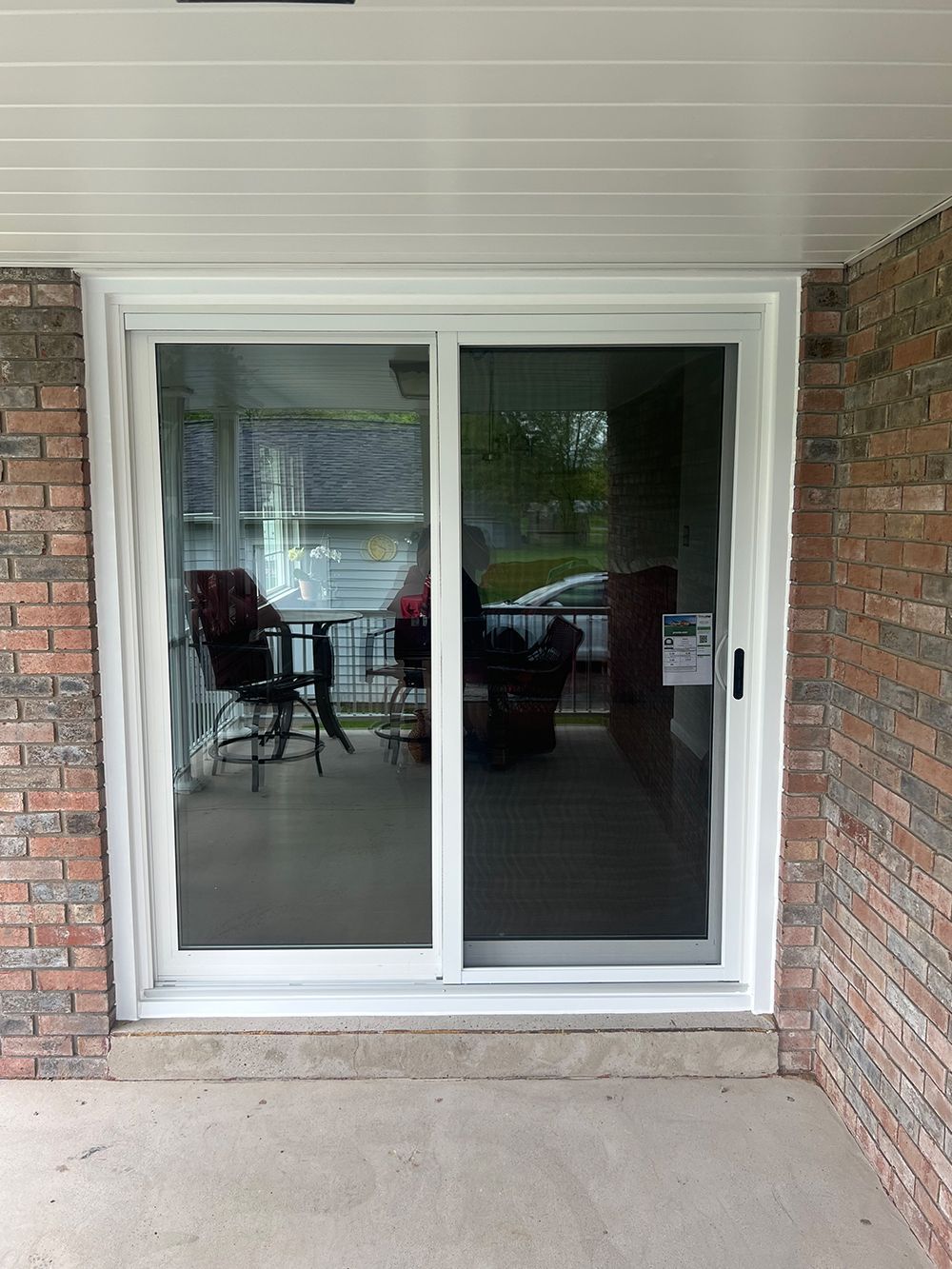 White sliding glass door on a brick wall, leading to a screened-in porch, concrete patio.