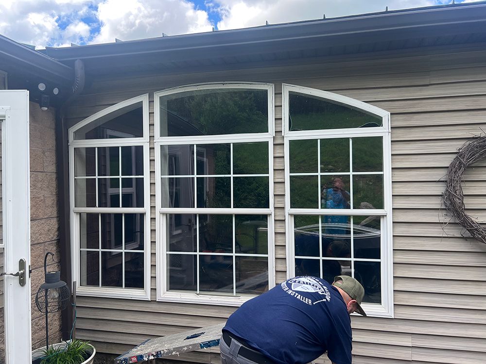 Man working on a large window with arched top, white frame, on a gray house with siding.