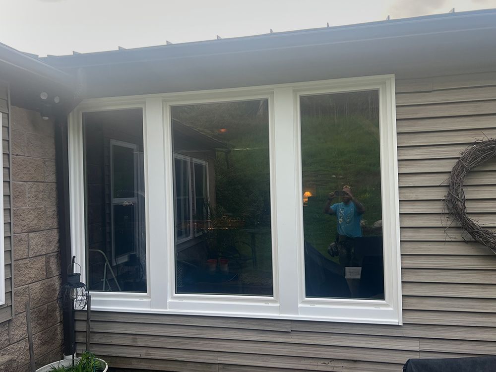 White-framed windows on a weathered building, reflecting outdoor scene with a person taking a photo.
