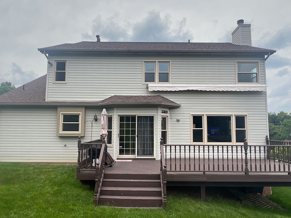 Back of a two-story house with a brown deck and a green lawn under an overcast sky.