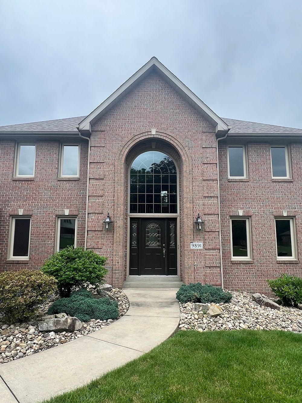 Brick house with arched entryway, dark door, large window, and small rectangular windows.