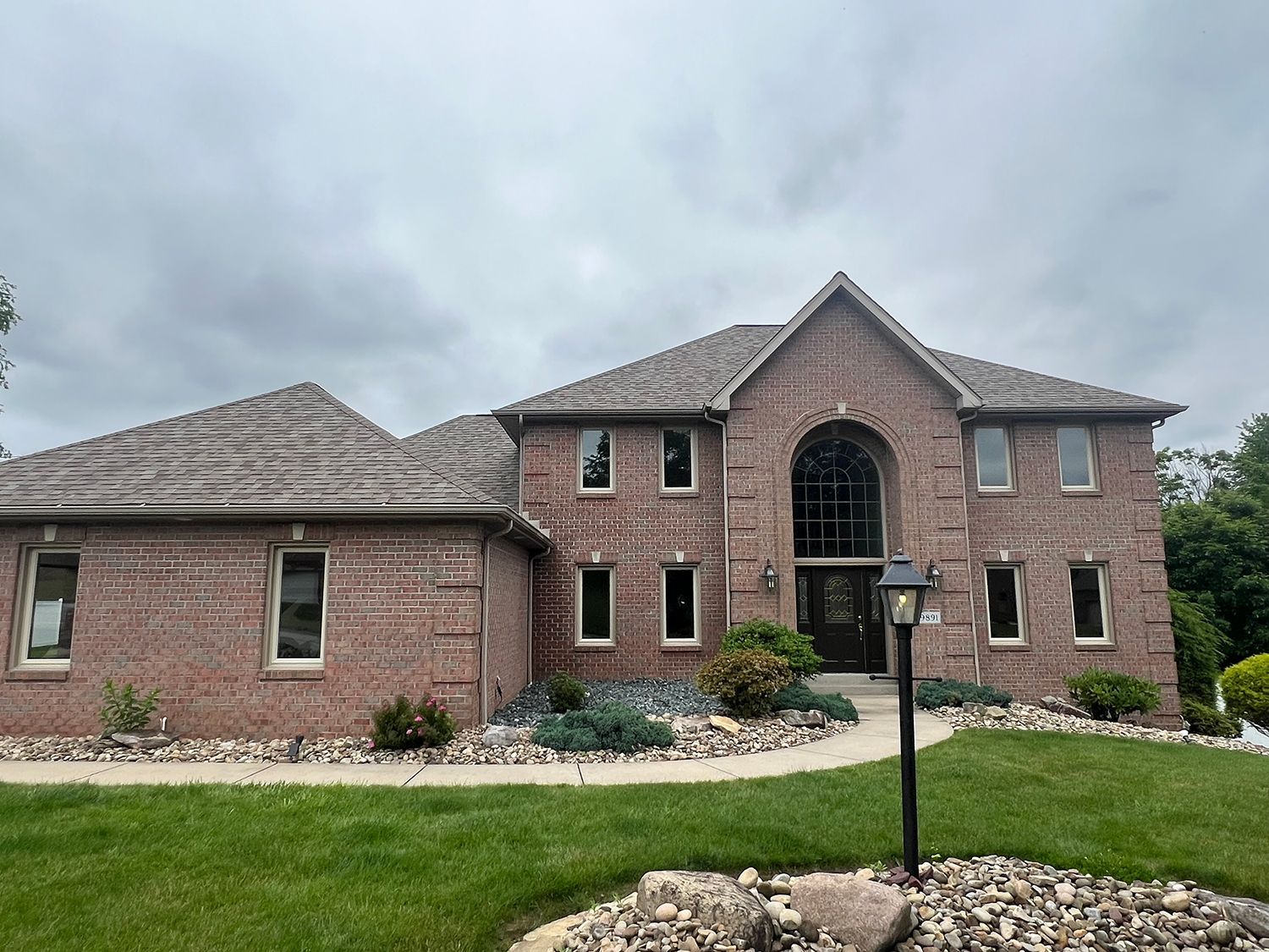 Brick two-story house with many windows, gray roof, cloudy sky, and green lawn.