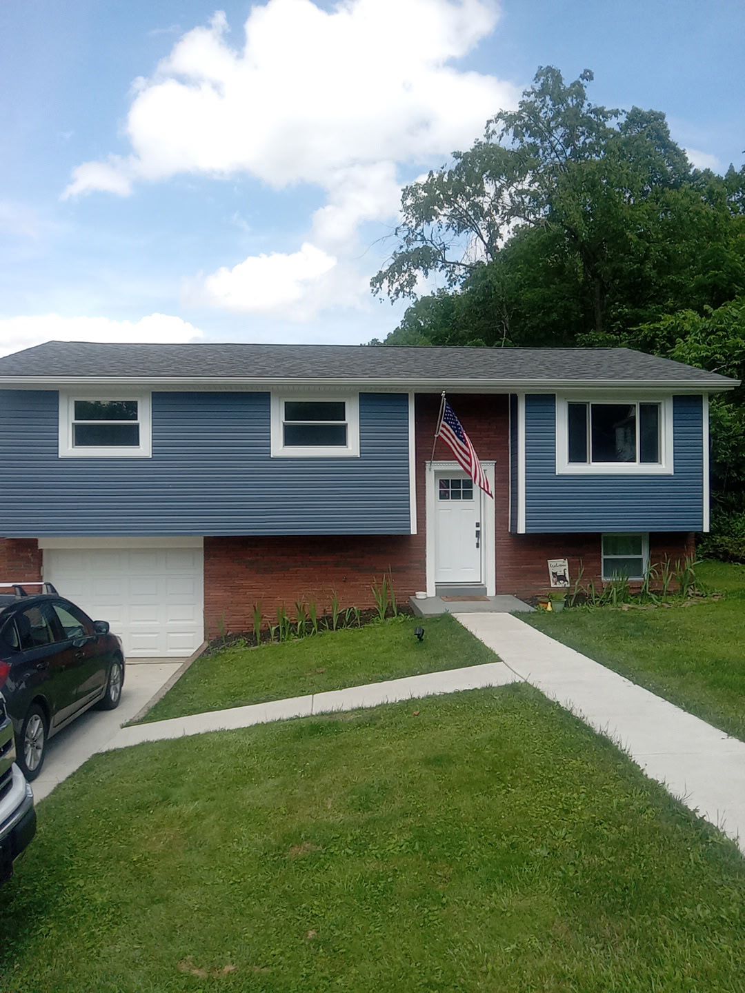 House with blue siding, brick, white door, windows, American flag, and green lawn.