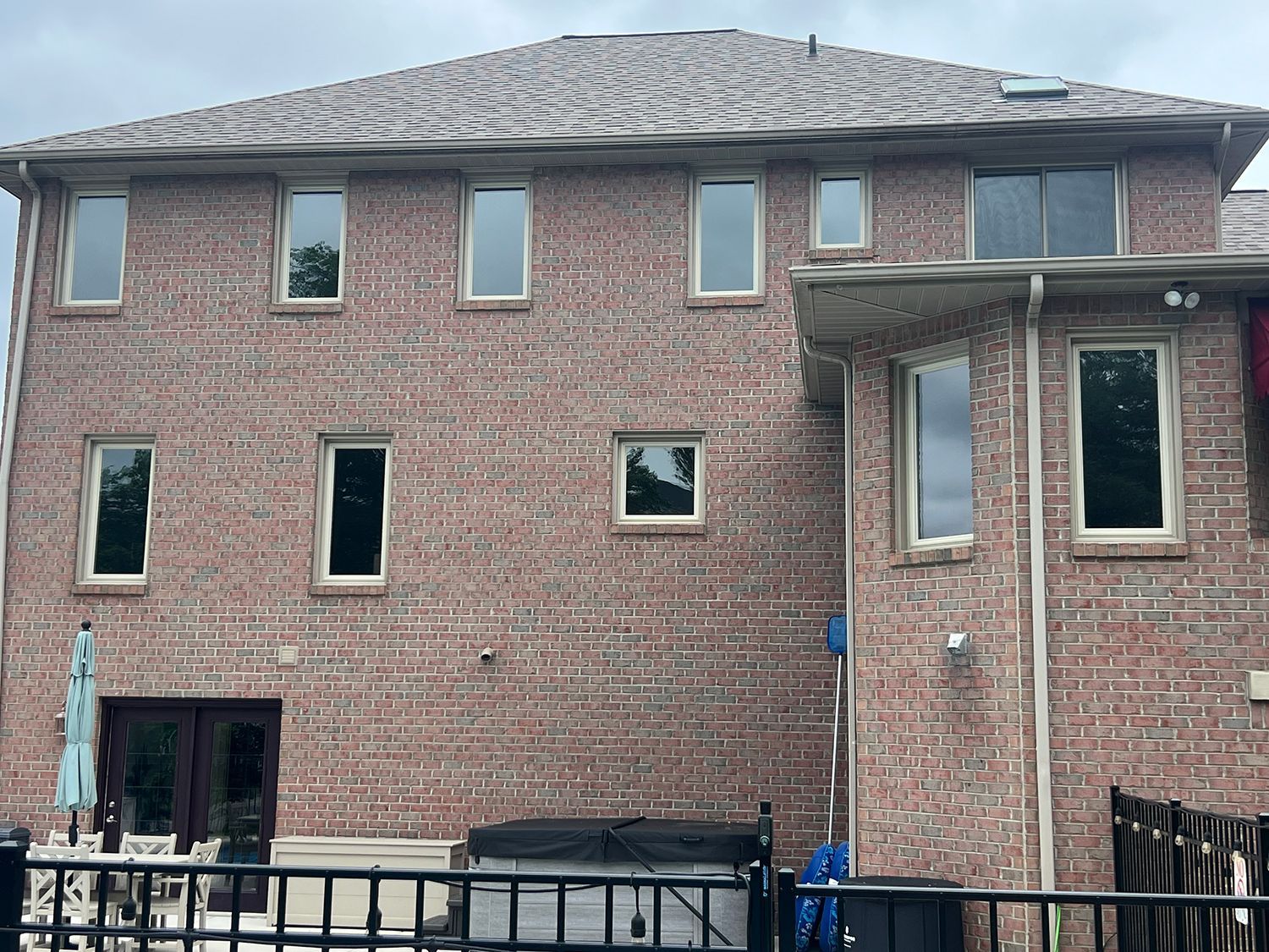 Two-story brick house with multiple windows and a brown shingled roof. Includes patio furniture.