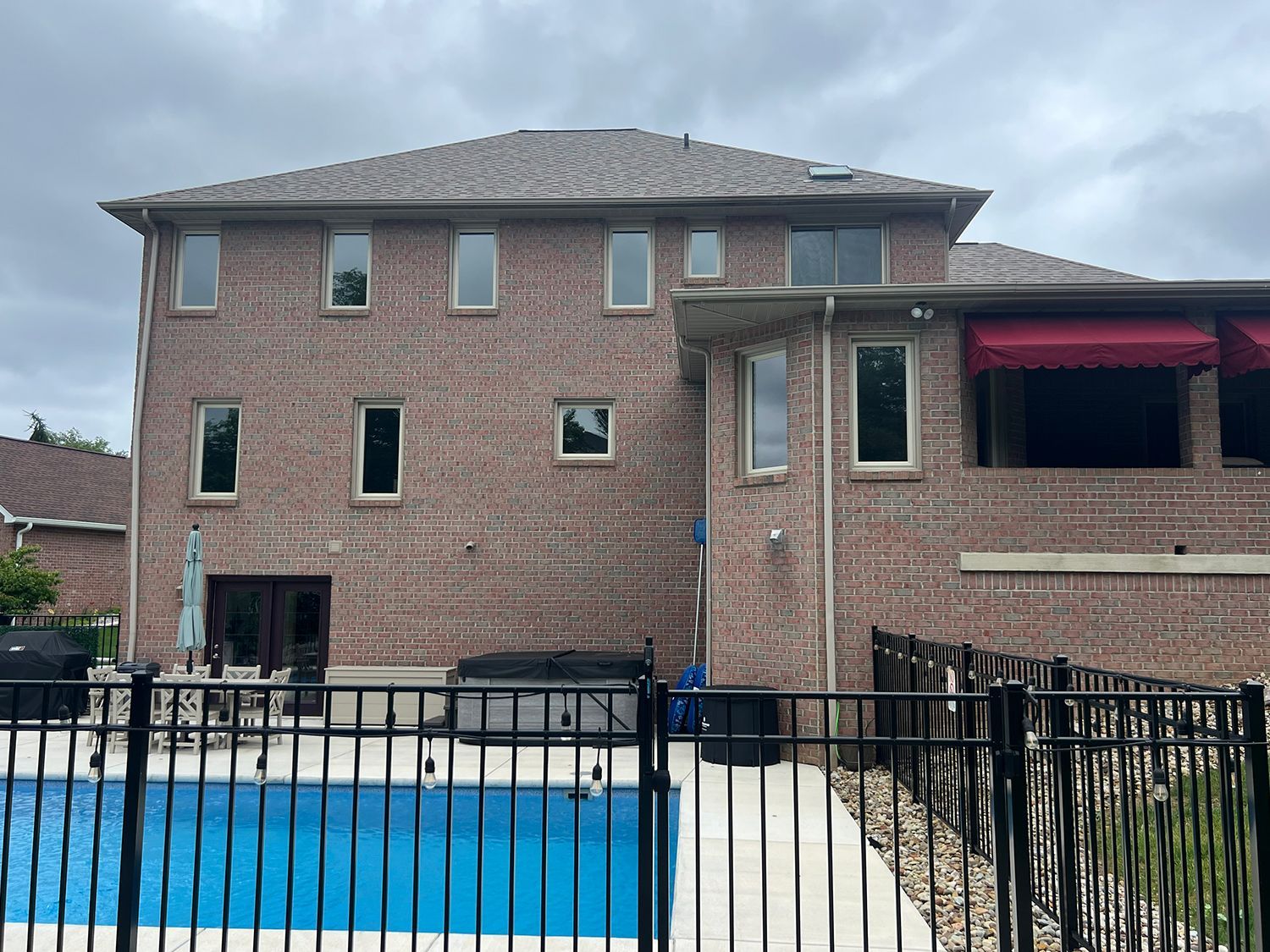 Brick house with pool and black fence. Cloudy sky.