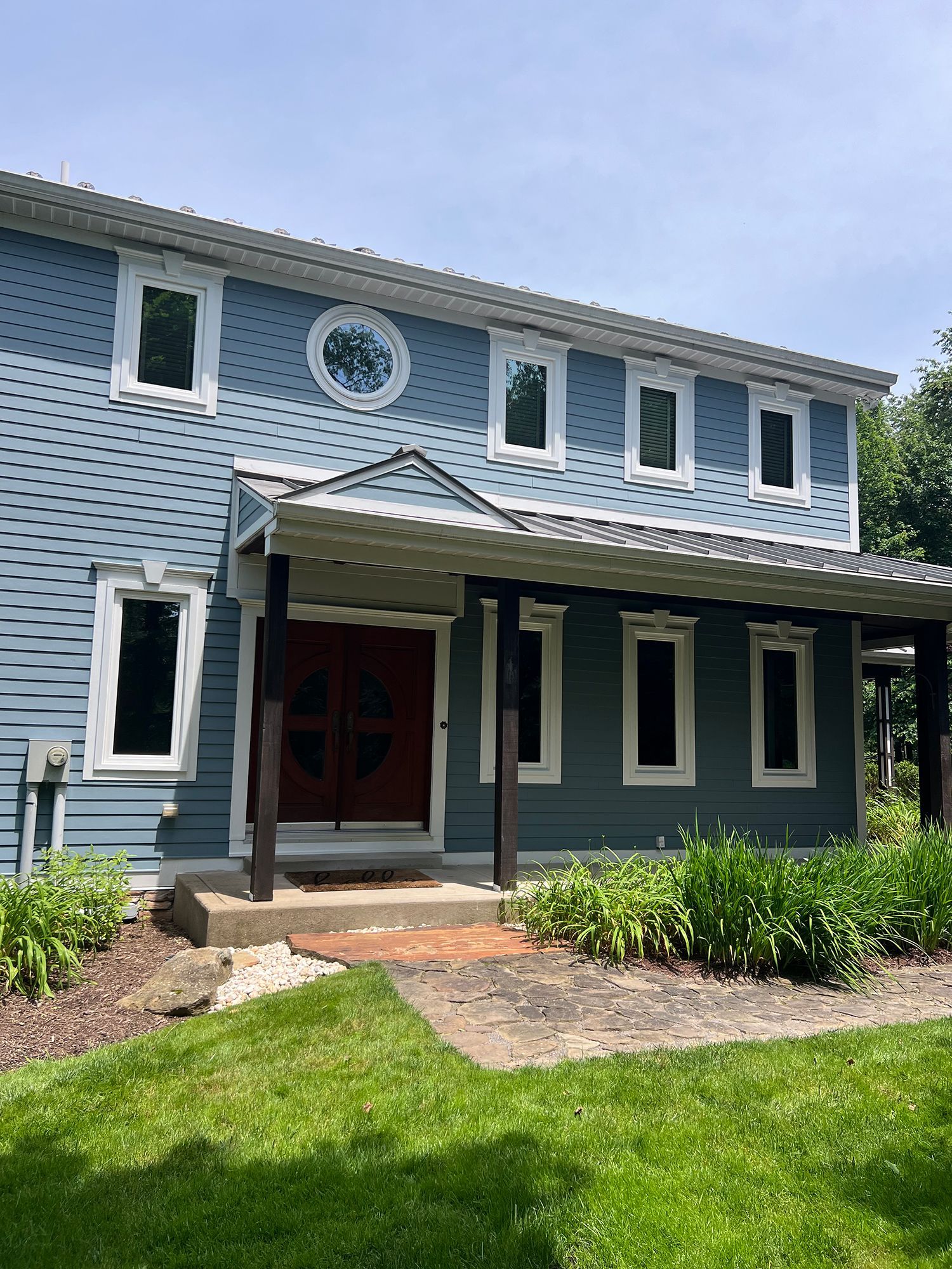 Blue house with white-trimmed windows and a covered entryway, in a green lawn.