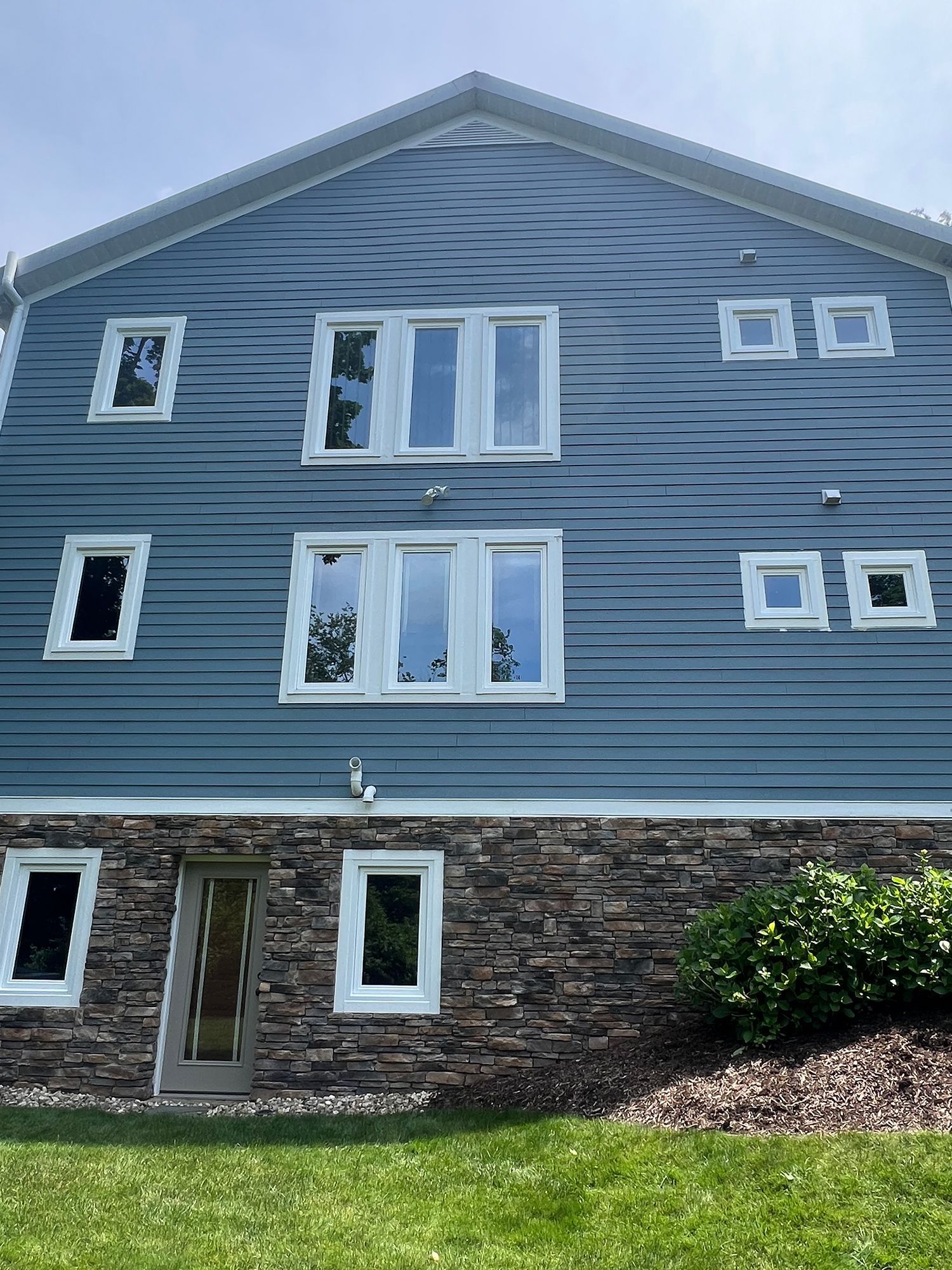 Blue siding on a two-story building with multiple windows and stone foundation; green grass in the foreground.
