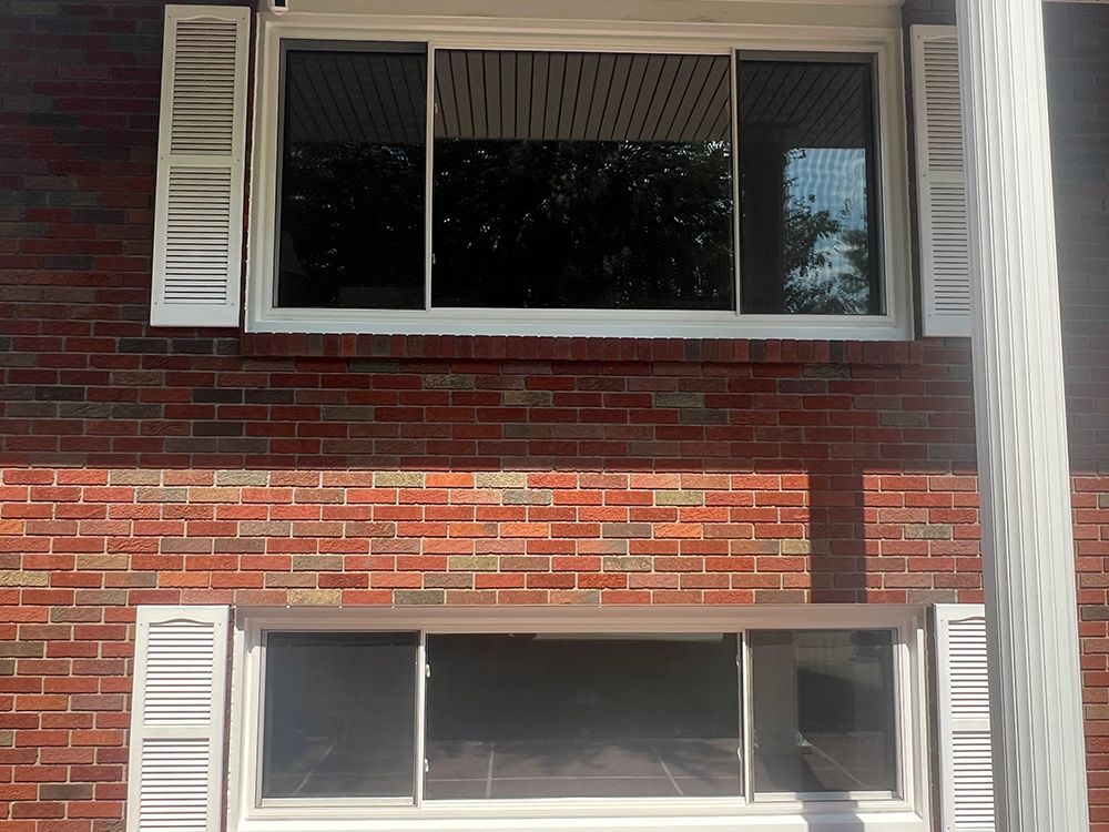 Two windows with white shutters on a brick building.