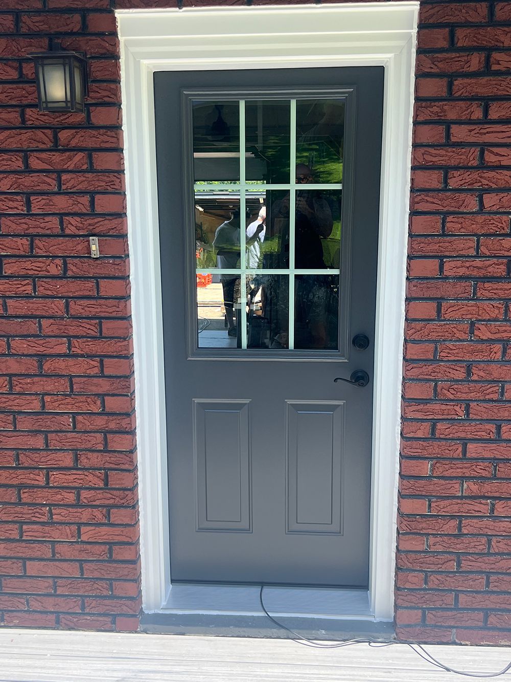 Grey door with glass panes, set in red brick with white trim.