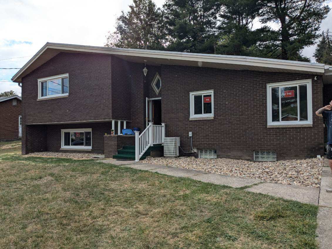 Brick house with white windows and a small front porch. Gravel and patchy grass in front.