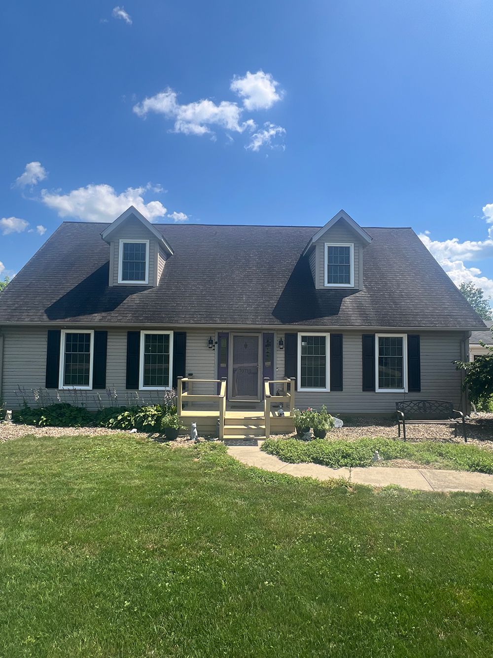 Ranch-style house with light siding, black shutters, and two dormer windows under a blue sky.