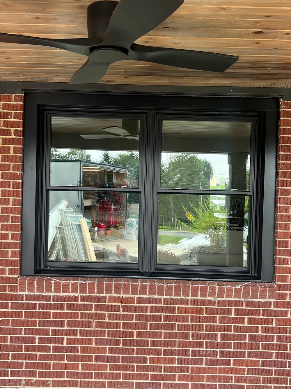 Black-framed window set in red brick wall. A ceiling fan is mounted above the window.