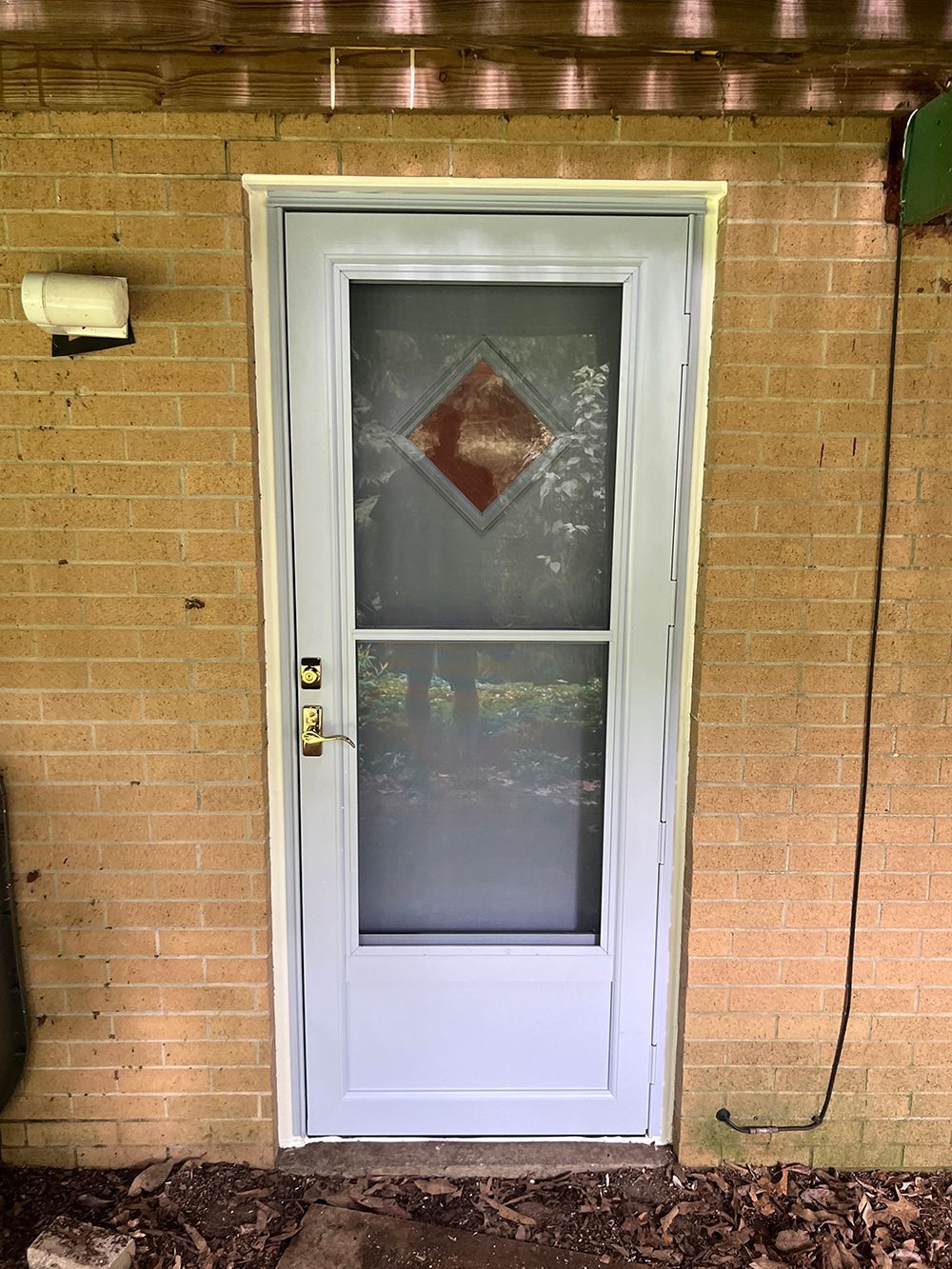 A light gray screen door with a diamond-shaped design on a brick wall.