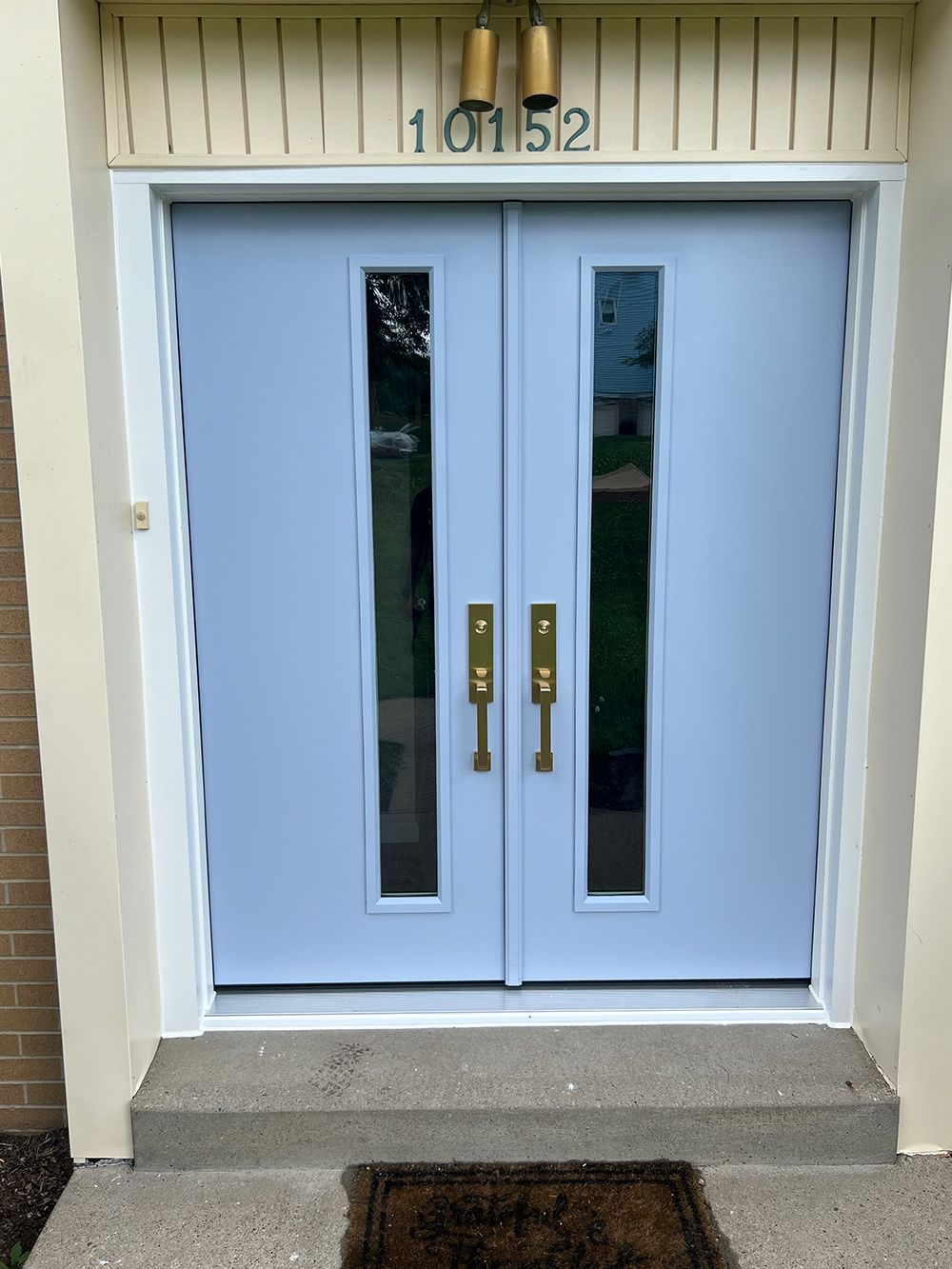 Light blue double doors with long glass panes and brass handles, under a house number.