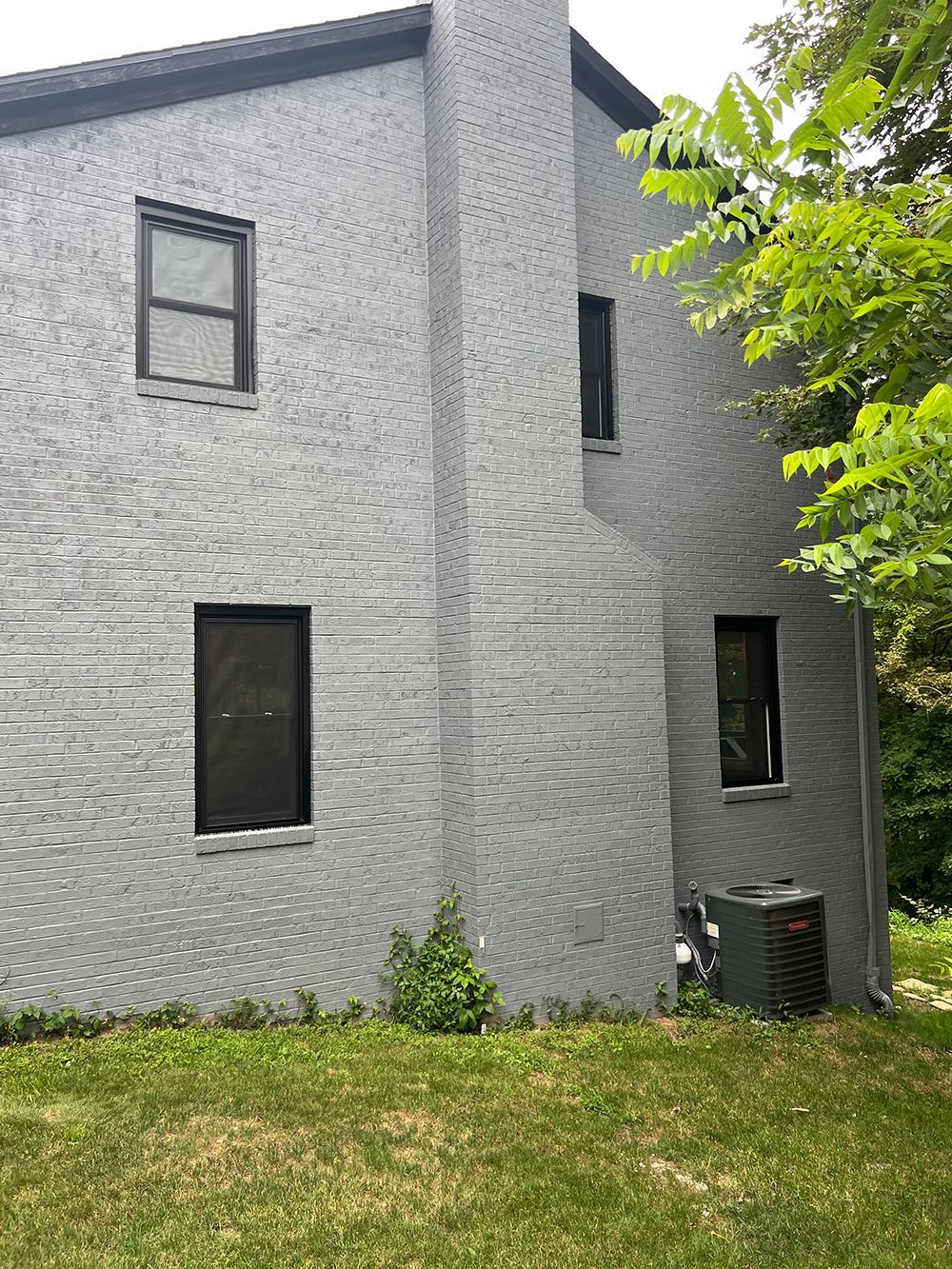 Gray brick house with black windows, air conditioner, and chimney.