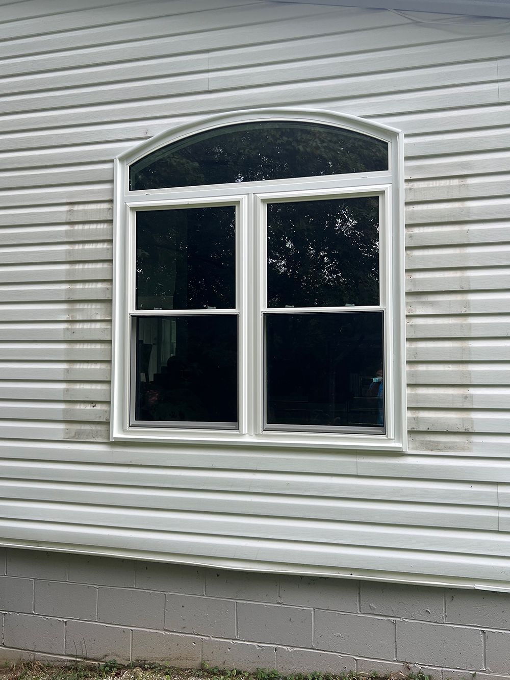 White arched window on a white vinyl-sided building. Green trees visible through the glass.