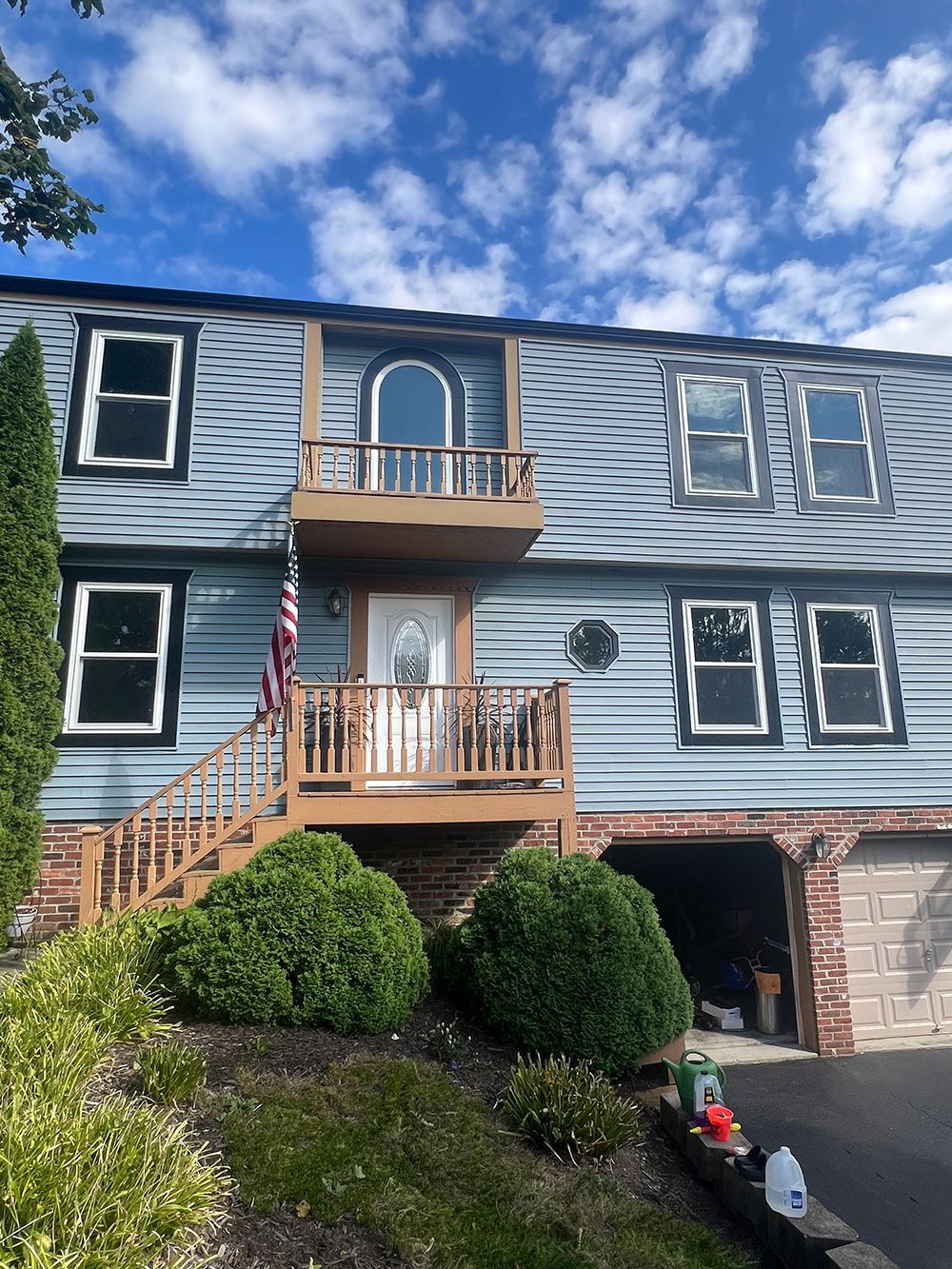 Blue house with a balcony and American flag; steps lead to the front door.
