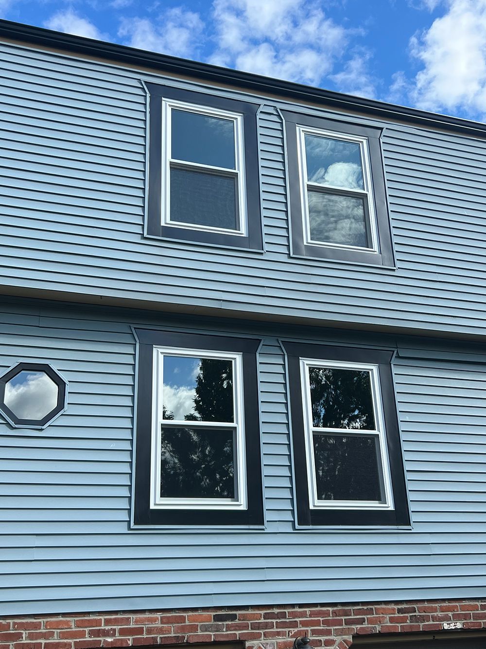 Blue house with dark-trimmed windows under a cloudy sky.