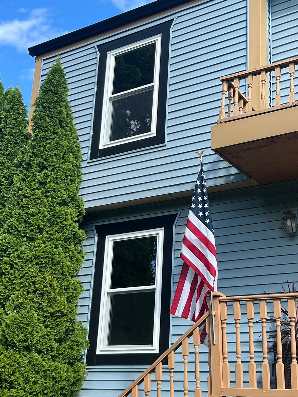 Blue house with black-trimmed windows, American flag, wooden stairs, and green tree.