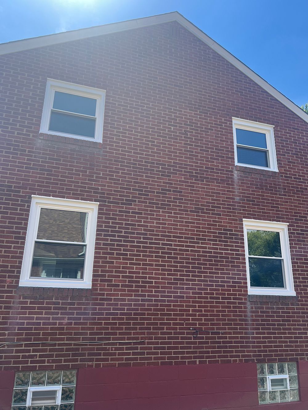 Red brick building with four windows and two basement windows; blue sky above.
