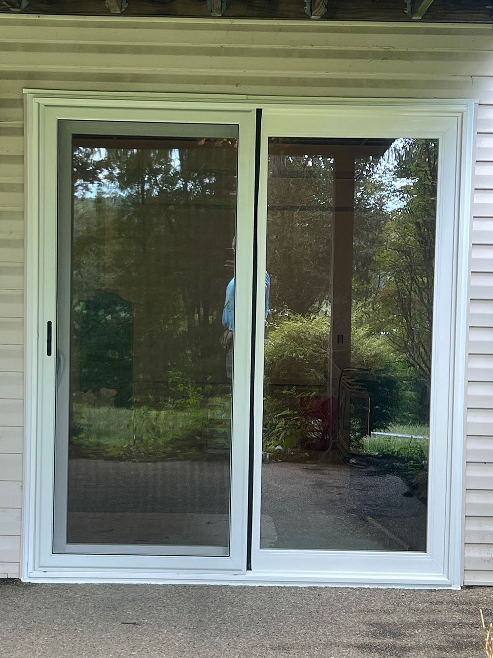 White sliding glass doors on a porch, reflecting a yard with trees and greenery.