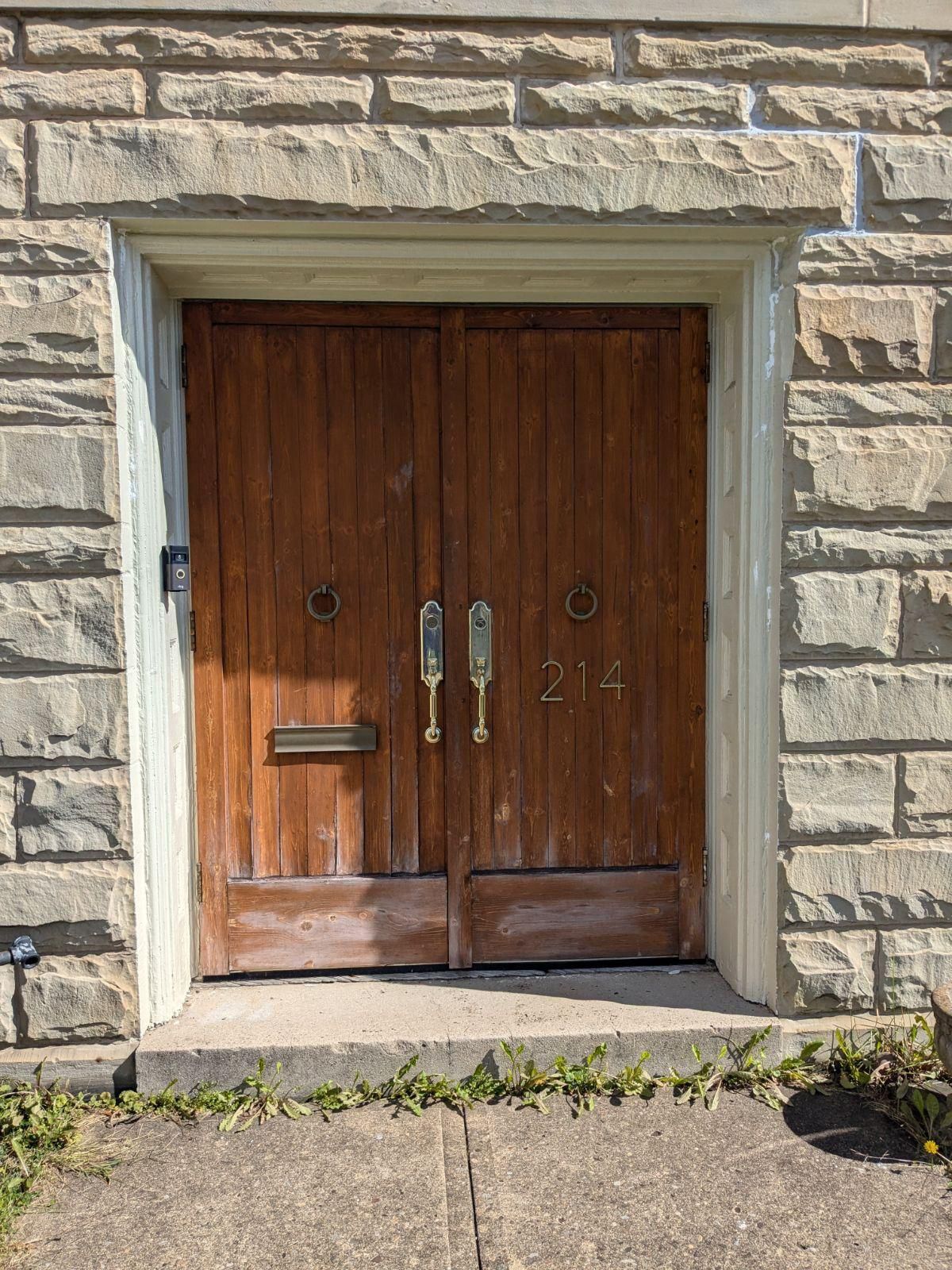 Brown wooden double doors in a stone doorway, with brass handles and a mail slot.