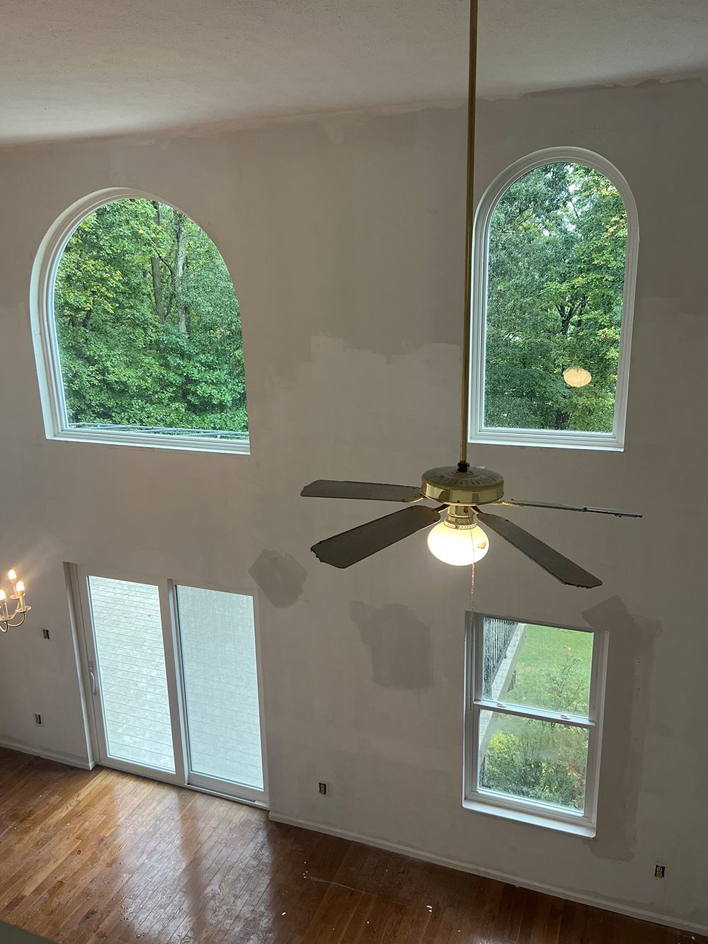 High-angle view of a white-walled room with arched windows, sliding glass doors, a fan, and wood flooring.