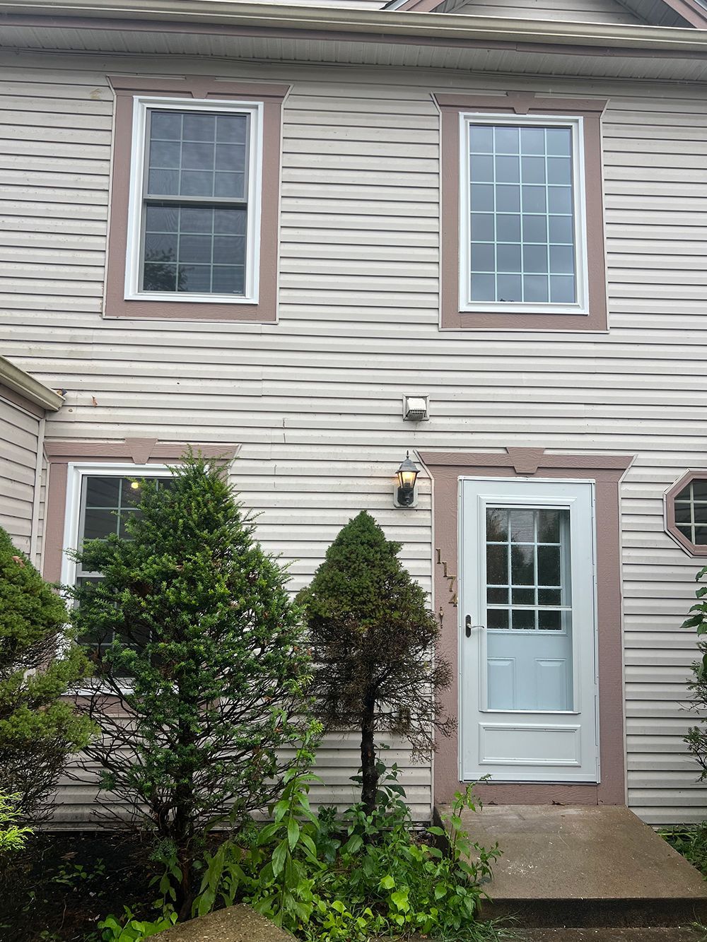 Beige building with white-framed windows and door, accented with brown trim. Green shrubbery in front.